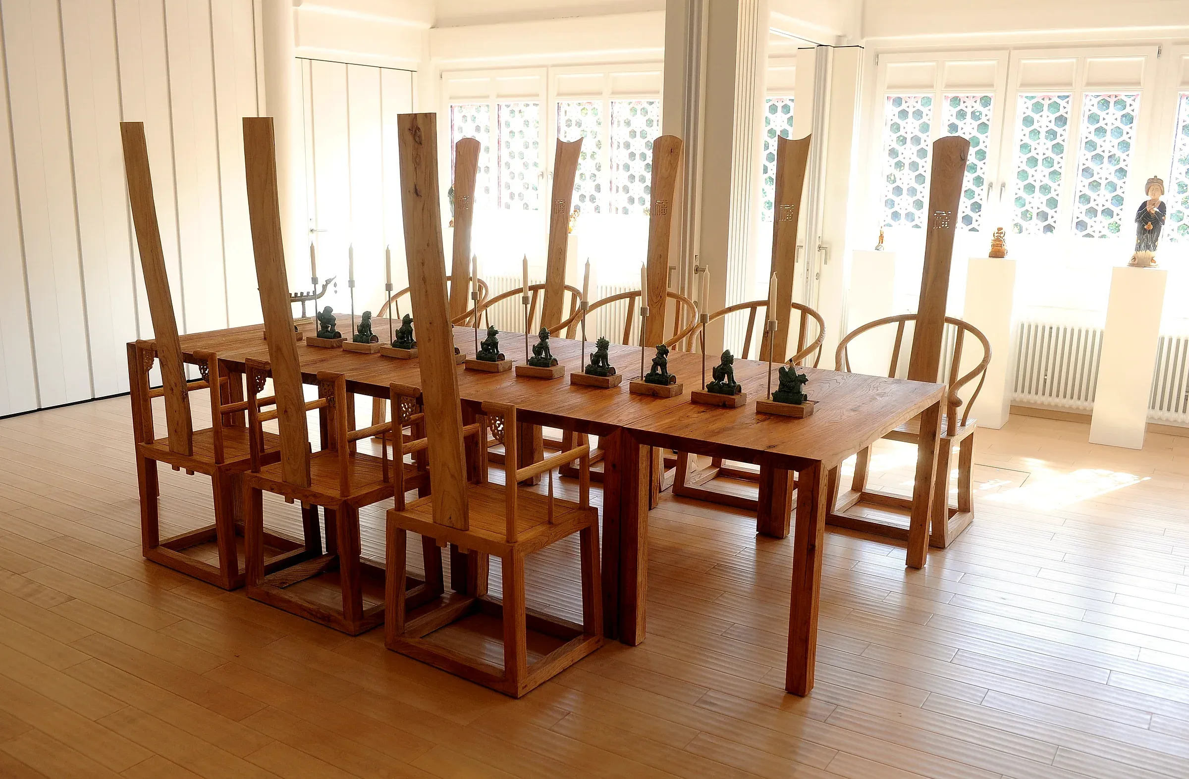Massive Ming-Stühle an einer langen Holztafel vor hellen Gitterfenstern.